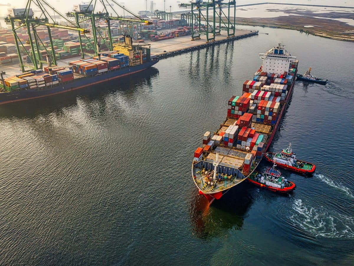 Containerschiff wird von Schleppern an einem Hafenterminal manövriert